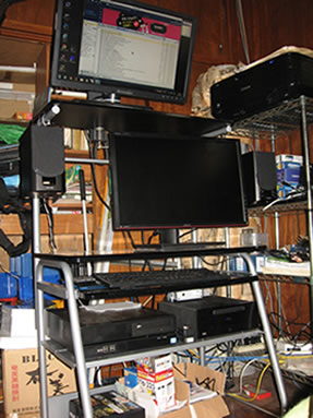 パソコンラック周り。上下2台のモニターの下には、A社の静音PC（左）と弊社無音PC（右）が並ぶ 画像